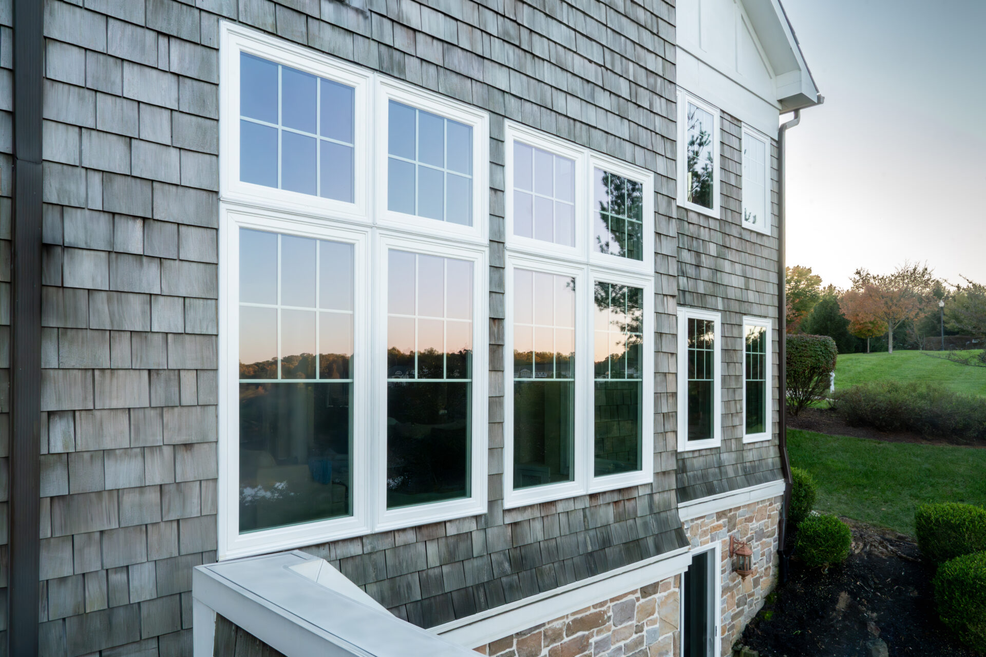 Potomac HP windows in white reflecting a sunset on a Cape Cod-style home, showcasing exceptional clarity and design.